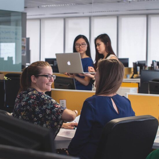 Three women are sitting at a table with laptops.