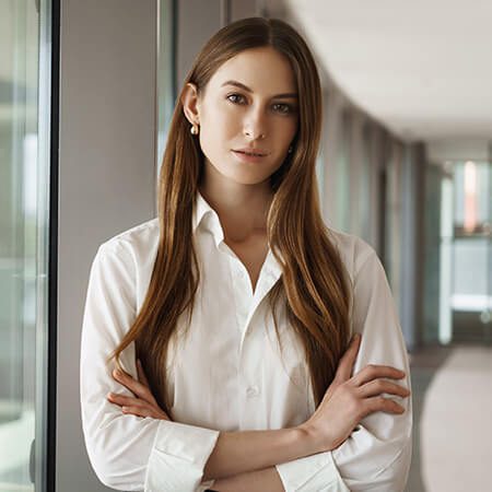 A woman standing in front of a window with her arms crossed.