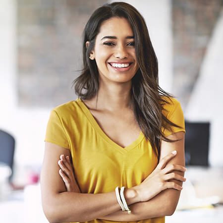 A woman in yellow shirt smiling with her arms crossed.