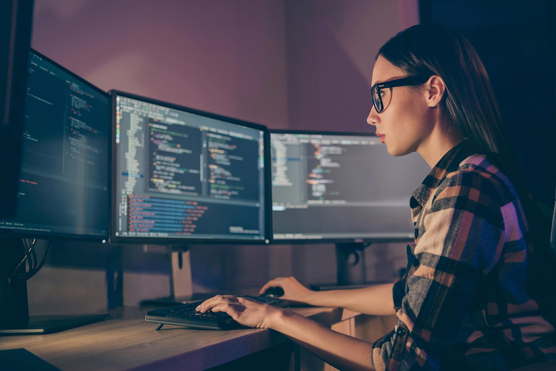A person sitting at a desk with three computer monitors.