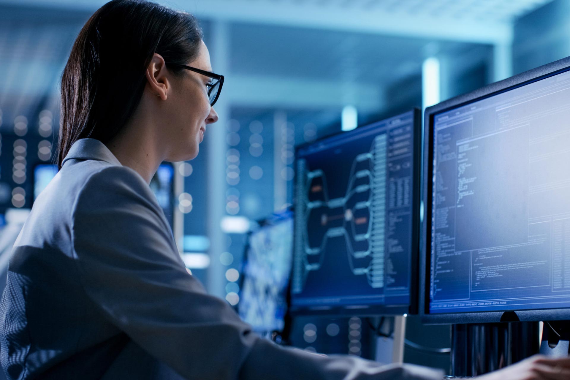 A woman sitting at a desk in front of two computer monitors.