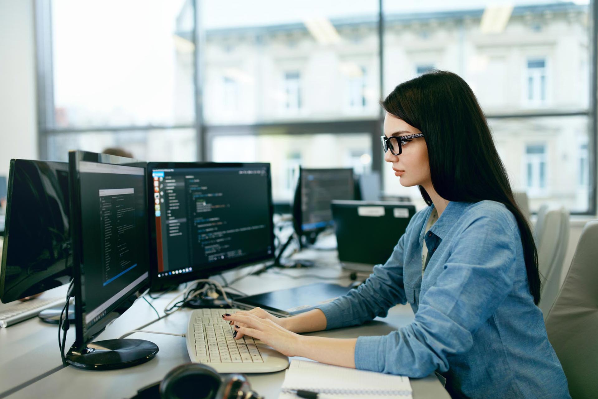 A woman sitting at a desk with two computers.