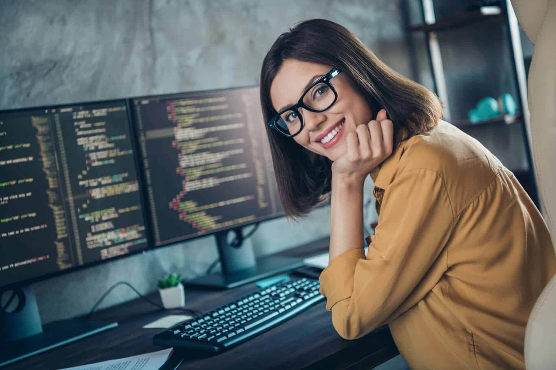 A woman sitting at her computer desk with two monitors.