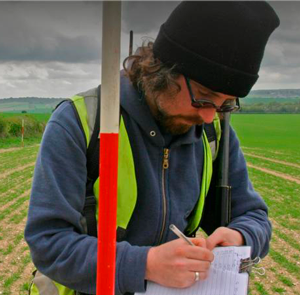 A man writing on paper in front of an open field.